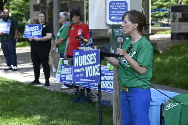 Photo of a nurse speaking at a podium with a sign thaty says "Nurses Deserve a Voice"